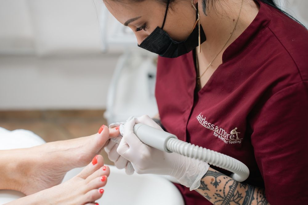 Ein Techniker in weinroter Uniform führt eine Pediküre mit einem Gerät durch.